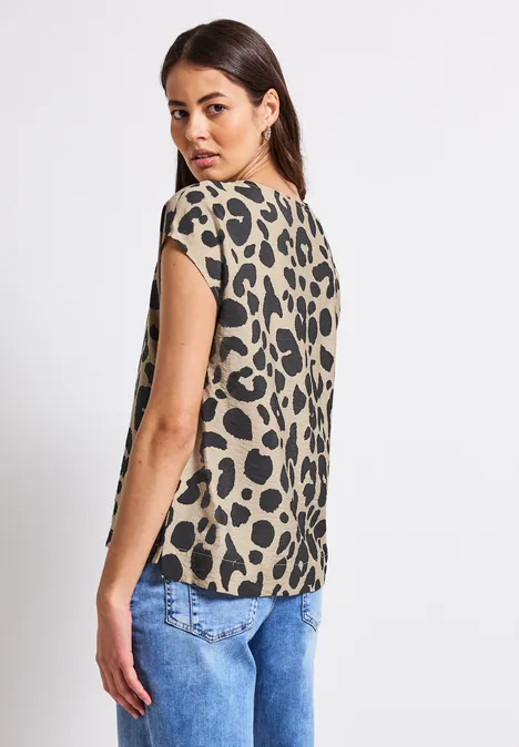 Frau mit Leopardenmuster-Top und Jeans schaut über die Schulter.